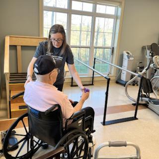 A caregiver assists an elderly individual in a wheelchair during a physical therapy session.