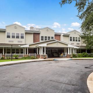 A large residential building with a driveway and surrounding trees under a clear blue sky.