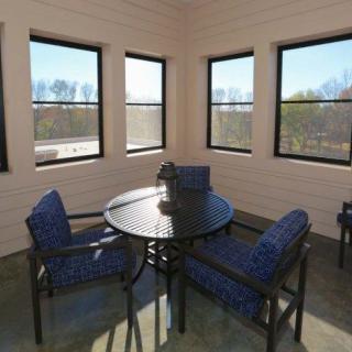 A cozy indoor patio area with a round table and cushioned chairs surrounded by windows.