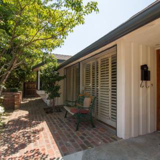 A sunny exterior view of a house with a brick pathway and surrounding trees.