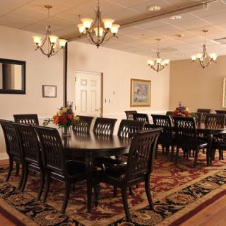 An elegant dining room with formal setup, featuring chandeliers and a decorative rug.