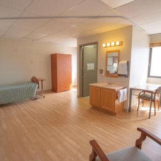 An interior view of a hospital room with a bed, seating area, and medical equipment.