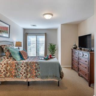 A cozy bedroom featuring a neatly made bed, a dresser with a TV on top, and soft lighting.