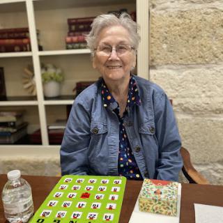 An elderly woman enjoying a game of bingo, smiling at the camera.