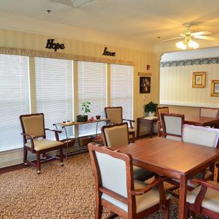 A cozy dining area with wooden tables and chairs, carpeted flooring, and decorative elements including wall art and plants.