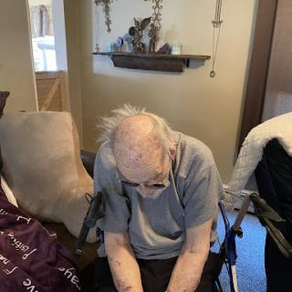 An elderly person sitting in a wheelchair, appearing thoughtful or reflective in a cozy indoor setting.