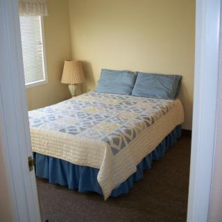 A cozy bedroom with a neatly made bed, complete with pillows and a quilt, beside a lamp and window.