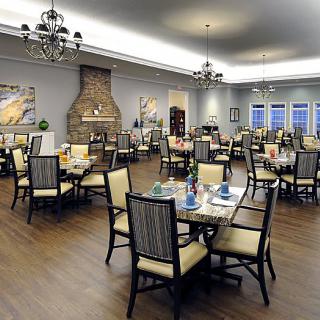An elegant dining room with neatly arranged tables and chairs, featuring chandeliers and a fireplace.
