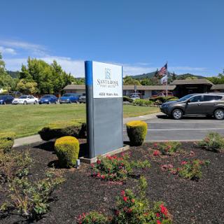 A clear view of a building's sign in front of a well-maintained landscape with cars parked nearby.