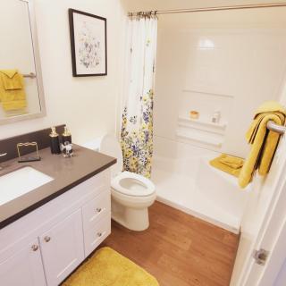 A neatly organized bathroom with yellow accents featuring a shower, sink, and toilet.