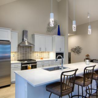 A modern kitchen featuring stainless steel appliances, a spacious countertop with bar stools, and stylish pendant lighting.