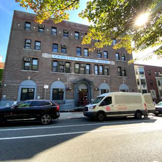 A view of a brick building with vehicles parked in front on a sunny day.
