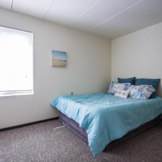 A cozy and minimalist bedroom featuring a well-made bed with blue bedding and a window that allows natural light to fill the space.