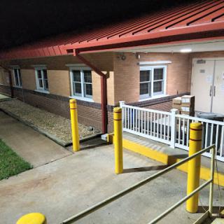 Exterior view of a commercial building at night, featuring yellow safety poles and a paved walkway.