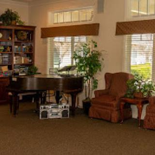 A cozy living room with a piano, armchair, and bookshelf by the windows.