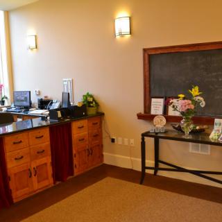 A cozy reception area featuring a wooden desk, flowers, and a chalkboard.
