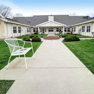 A pathway leading to a building, flanked by grass and a bench.