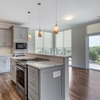 A modern kitchen with an open layout, featuring pendant lighting and hardwood floors.