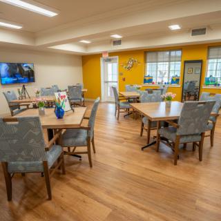 A cozy dining area with several tables and chairs, a television on the wall, and bright yellow accent walls.