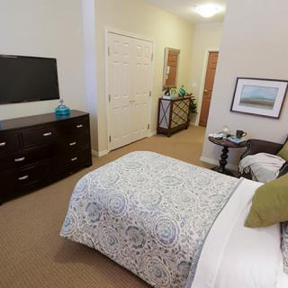 A cozy bedroom with a patterned bedspread, television, and dresser.