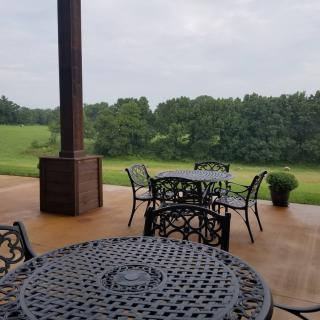 A serene patio overlooking lush greenery with metal tables and chairs under an overcast sky.