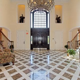A luxurious foyer with a grand chandelier, marble flooring, and two elegant staircases.