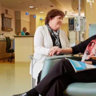 Two individuals sitting in a hospital setting, engaging in conversation and support.