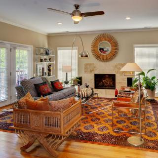 A cozy living room featuring a sofa, armchairs, and a colorful rug centered around a fireplace with decorative elements and houseplants.
