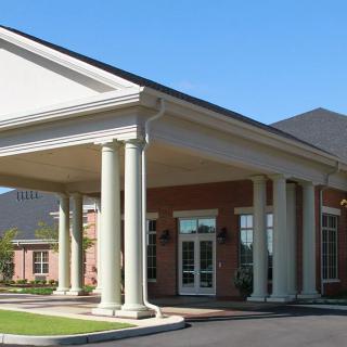 A brick building with a grand entrance featuring large columns and a covered canopy.
