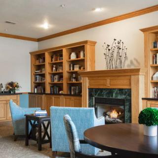 A cozy library with comfortable seating, bookshelves, and a warm fireplace.