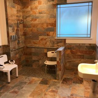 An accessible bathroom with a stone tile design, featuring a shower area, seat, and sink.