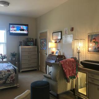 A cozy bedroom with furniture, a TV mounted on the wall, and soft lighting.