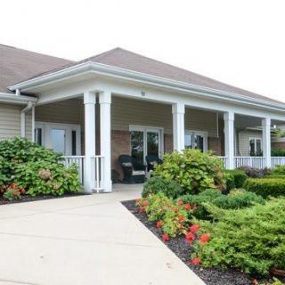 A single-story building with a front porch, featuring white columns, surrounded by landscaped gardens and shrubs.