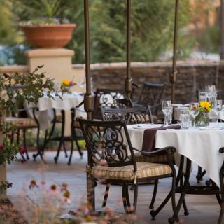An elegant outdoor patio setup at a restaurant with tables and chairs adorned with white tablecloths and floral centerpieces.