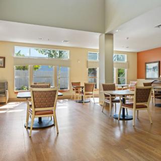 A bright and spacious dining area with tables and chairs, featuring large windows and hardwood flooring.