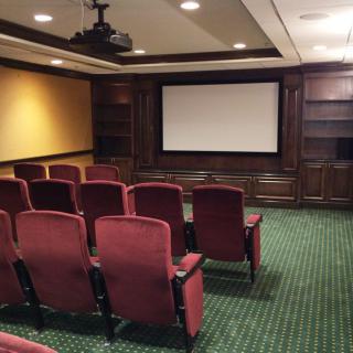 A cozy home theater with red upholstered seats and a large projector screen.