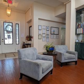 A cozy living room featuring two upholstered chairs, wooden flooring, and decorative elements on the walls and shelves.
