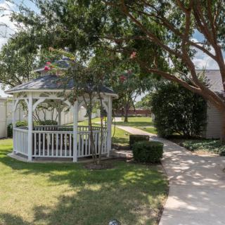 A serene garden featuring a white gazebo surrounded by trees and a manicured lawn.