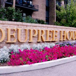 The entrance to a building labeled 'Deupree House' surrounded by vibrant pink flowers.