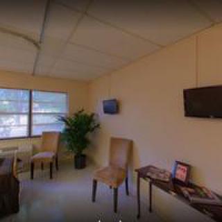 A small waiting room with chairs, a table, two televisions, and a window with natural light.