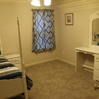 A simple bedroom with a bed, vanity dresser, and carpeted floor.