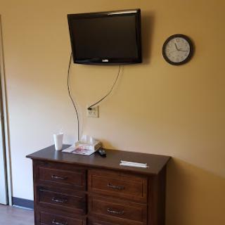 A simple room featuring a wall-mounted television and a clock above a wooden dresser.