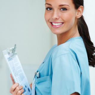 A smiling nurse holding a clipboard in a healthcare setting.