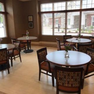 A cozy dining area with round tables and chairs, well-lit by large windows.