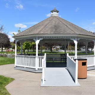 A charming gazebo in a park, surrounded by greenery under a clear blue sky.