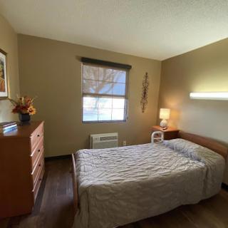 A cozy and simple bedroom featuring a bed, dresser, and a window with natural light.