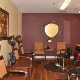 A cozy salon waiting area with chairs, hair dryers, and a large circular mirror on the wall.
