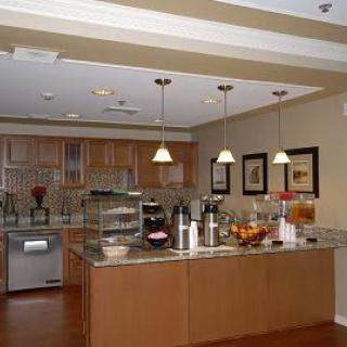 A modern kitchen interior featuring wooden cabinetry, a central island with pendant lighting, and various appliances and decor.