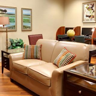 A cozy living room setup featuring a beige sofa with decorative pillows, surrounded by tasteful artwork and greenery.