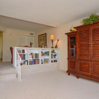 A cozy living room area featuring a bookshelf with various books and decorations, alongside wooden furniture and a warm lamp.